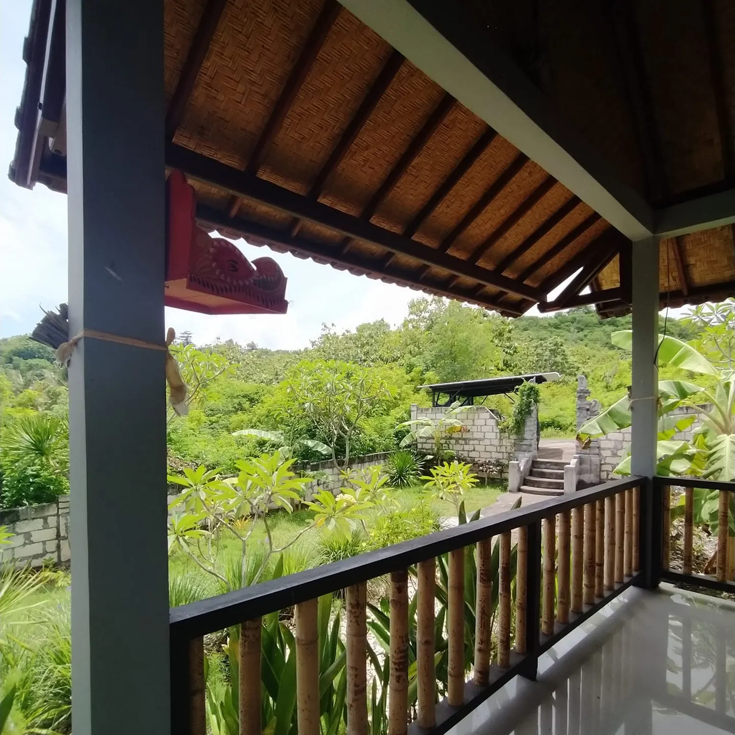 View from a covered veranda with a timber railing over green trees and shrubs