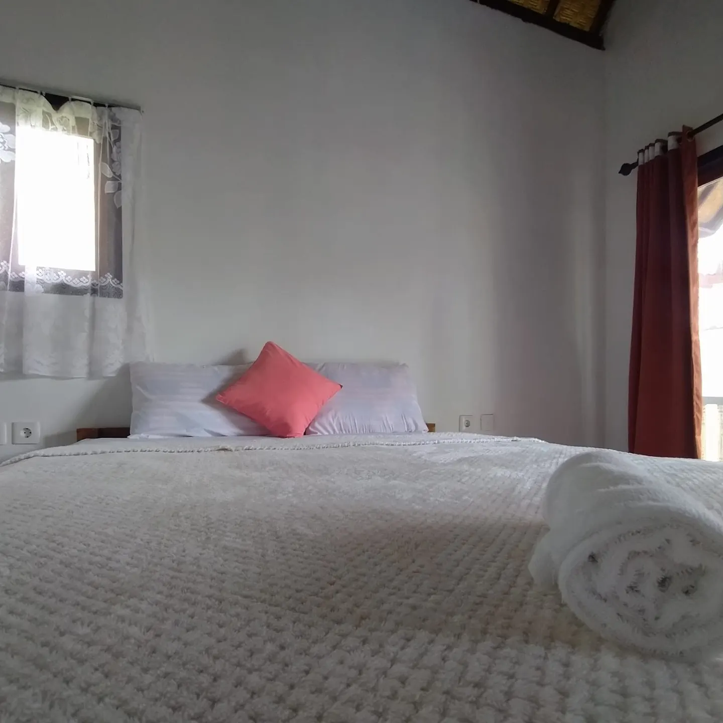 Double bed with white linen and a coral cushion under a window
