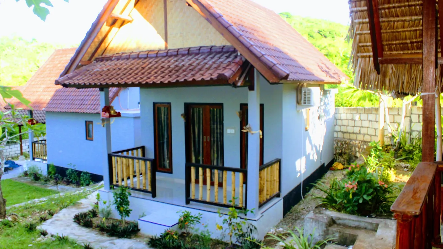 A white bungalow with a tiled roof and a small porch, surrounded by garden plants at Utamaru Homestay