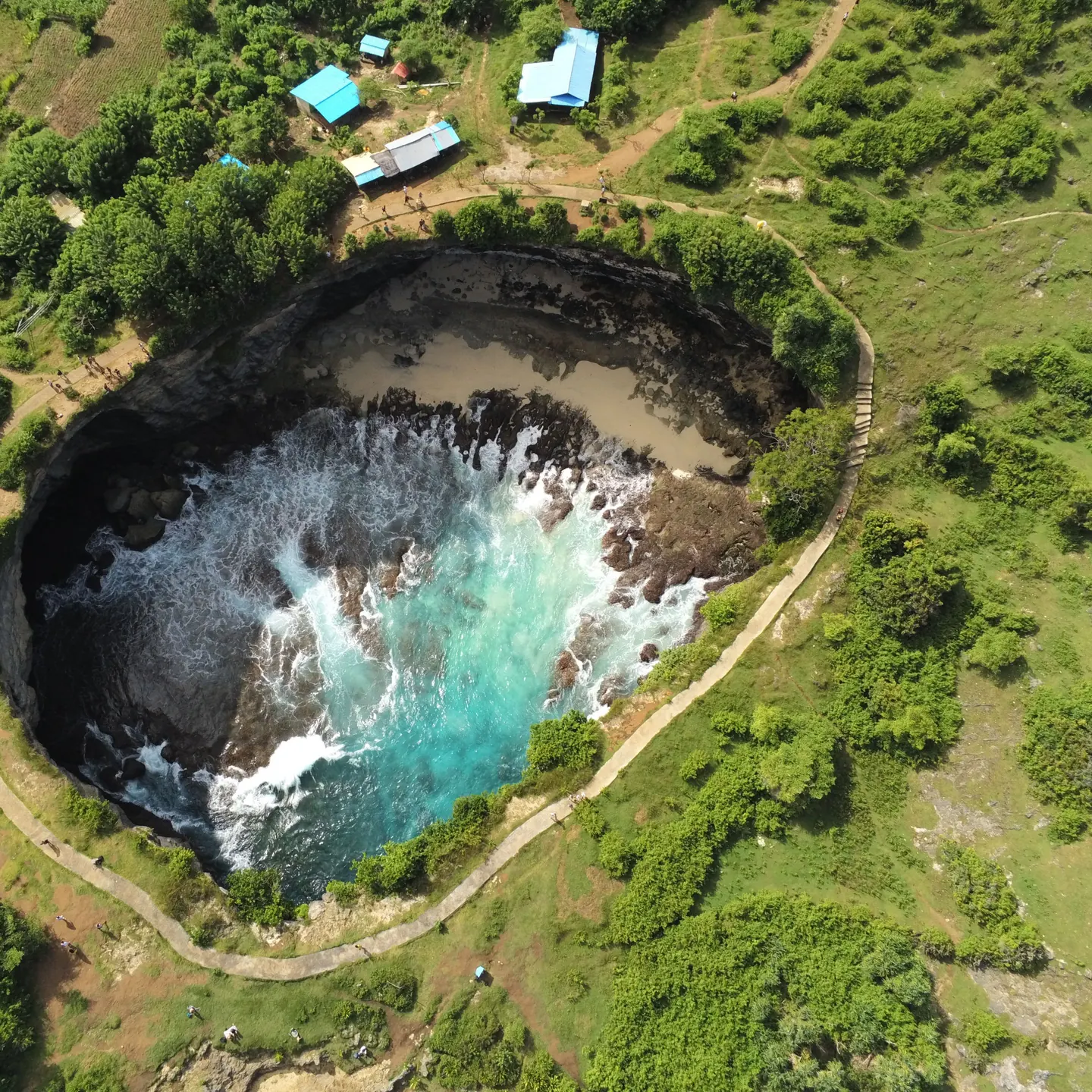 Aerial view of a rock pool beside the sea, ringed by a path