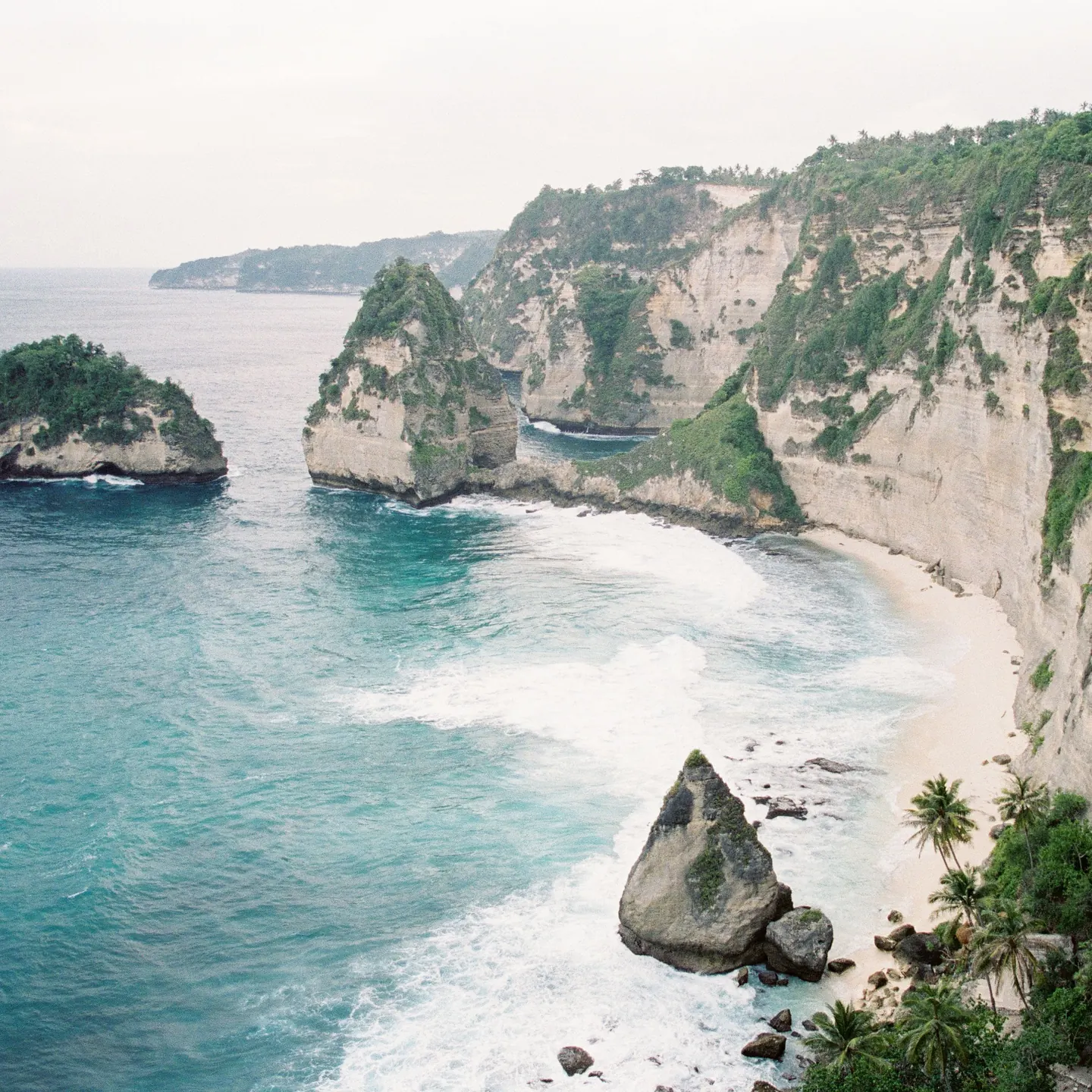 A curved beach below white cliffs, with rock islands in the sea
