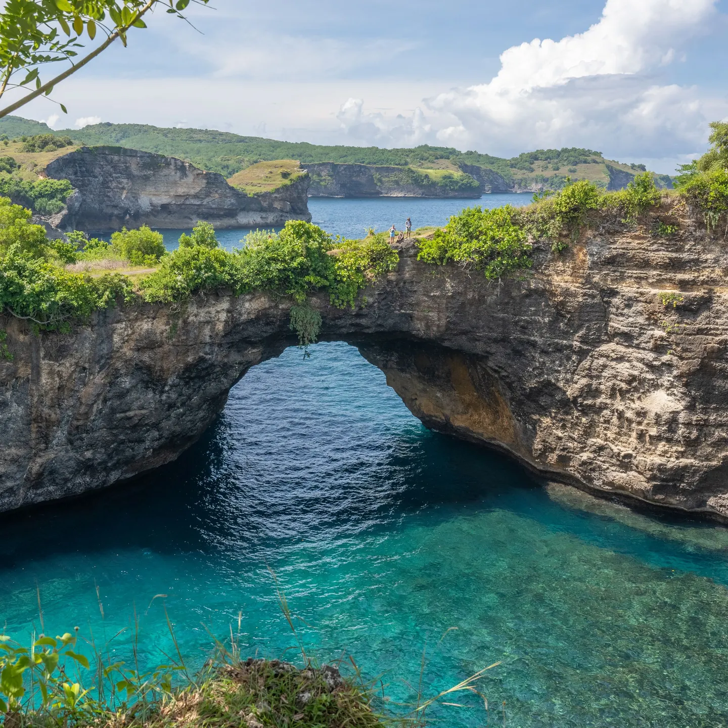 A natural rock arch over a round bay of blue water